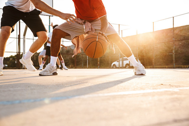 Un hombre con pantalones cortos grises y una camisa roja regatea una pelota de baloncesto.